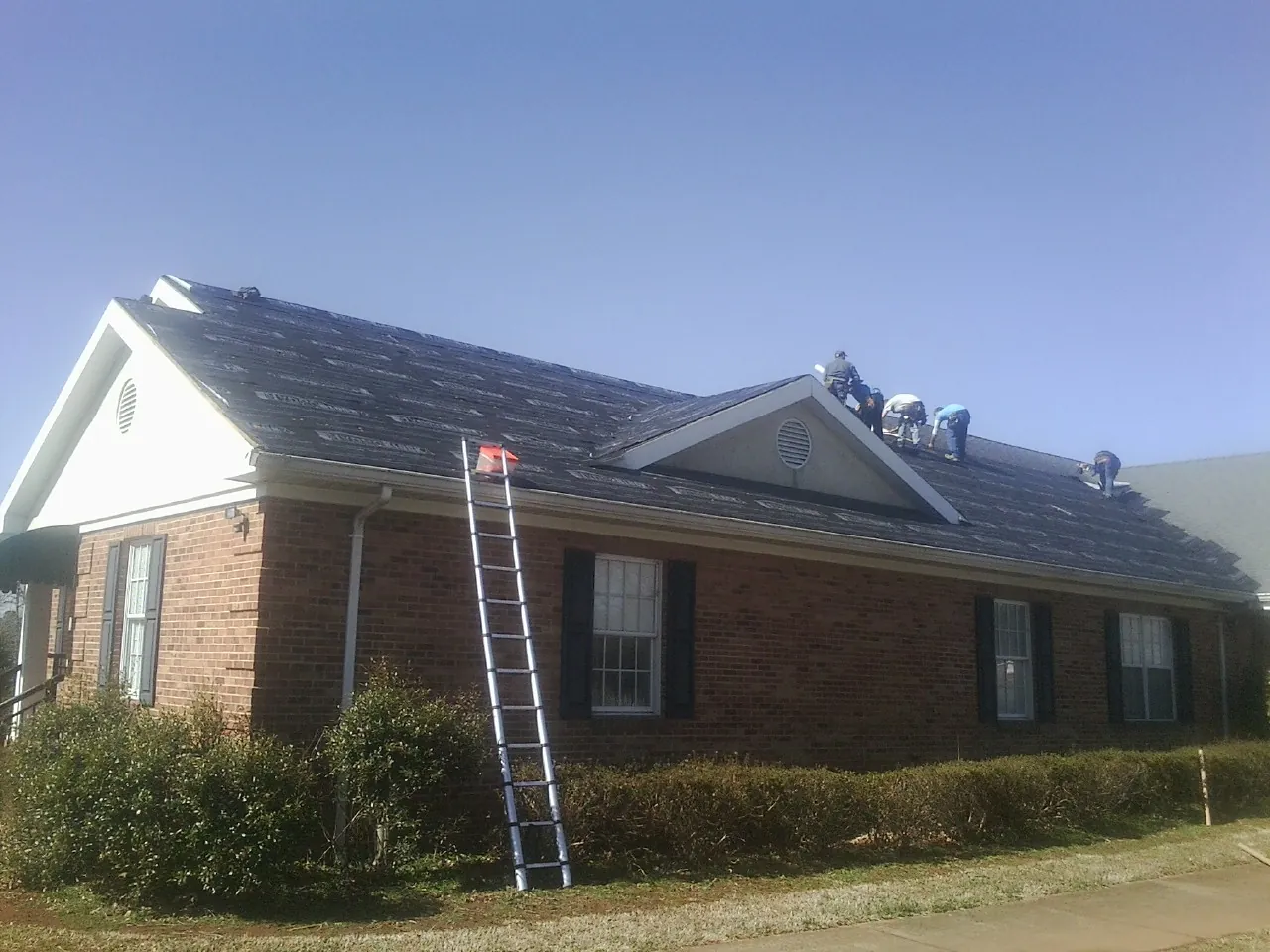 Crew tearing shingles off a brick ranch roof with a ladder set — Metal Roof Repair work by our crew in Duncan